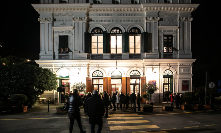 People entering a brightly lit building with a classic facade at night.