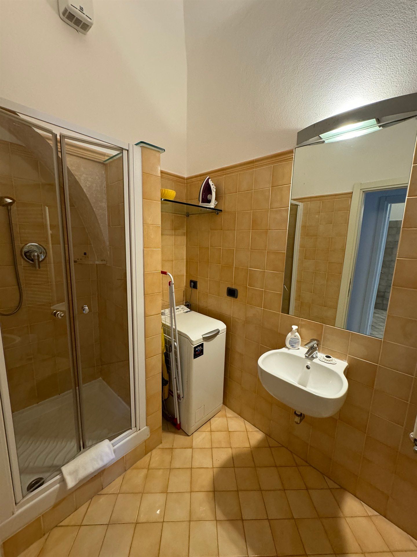A bathroom with a sink , washing machine , shower and mirror.