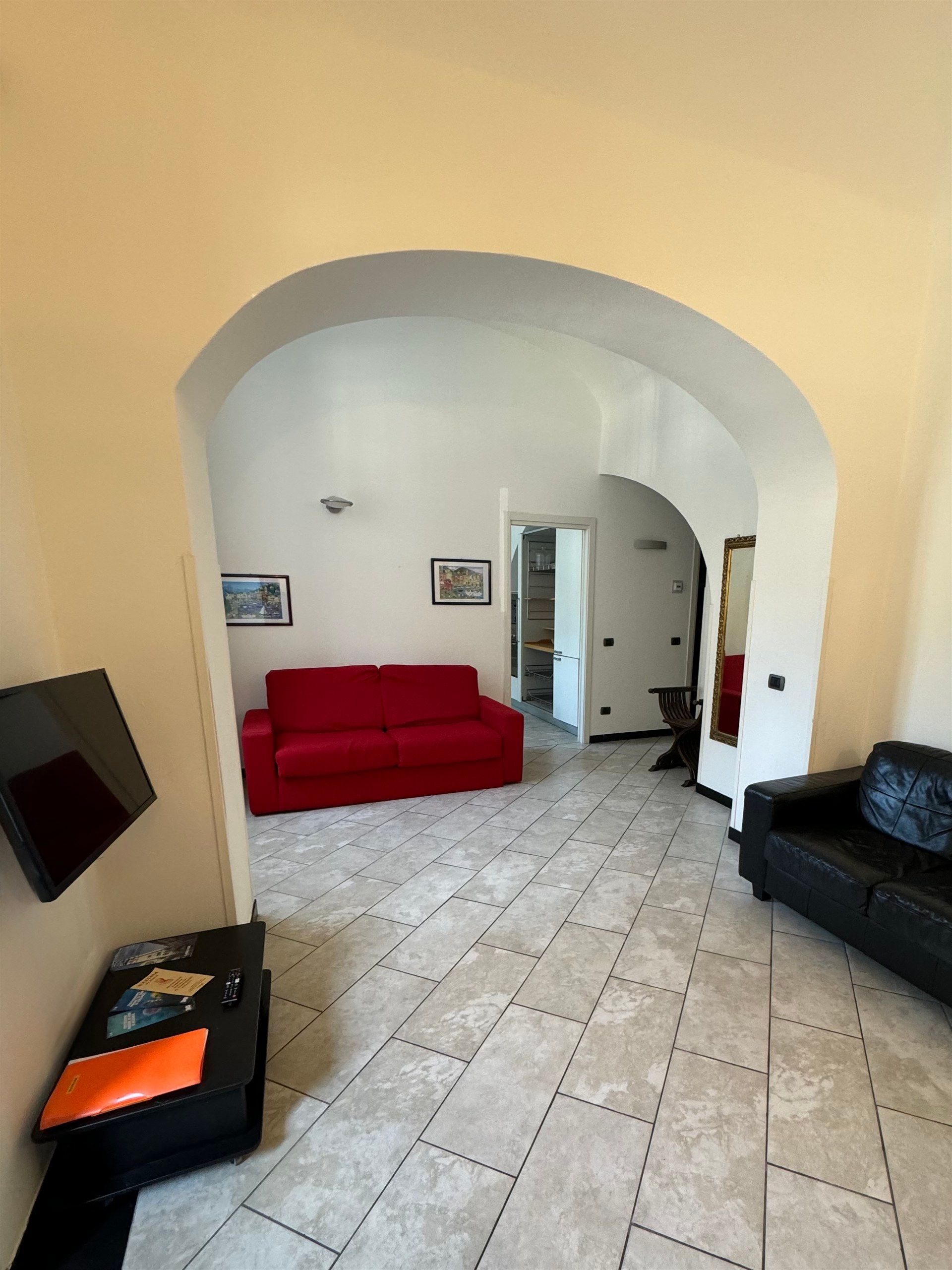 Interior view of a living space with a red sofa, black sofa, and tiled floor.