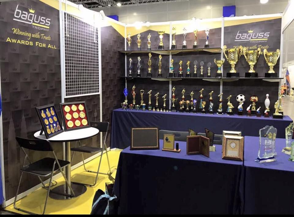 Display of Baguss Enterprise products at MGF 2017, KLCC — featuring trophies, medals, plaques, and crystal awards.