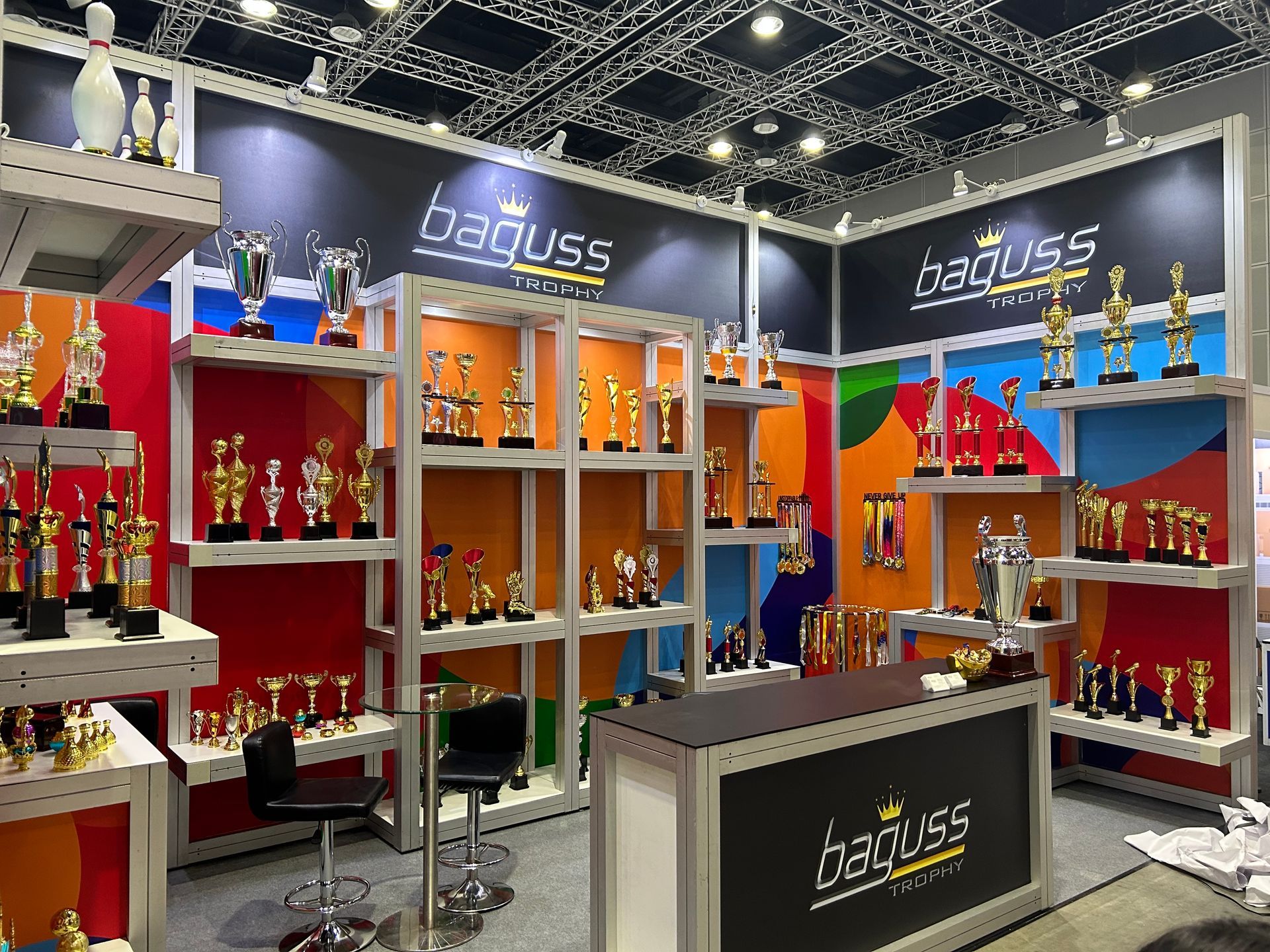 Full view of Baguss Enterprise booth at MGF 2023, KLCC — displaying trophies, medals, promotional items, and awards.