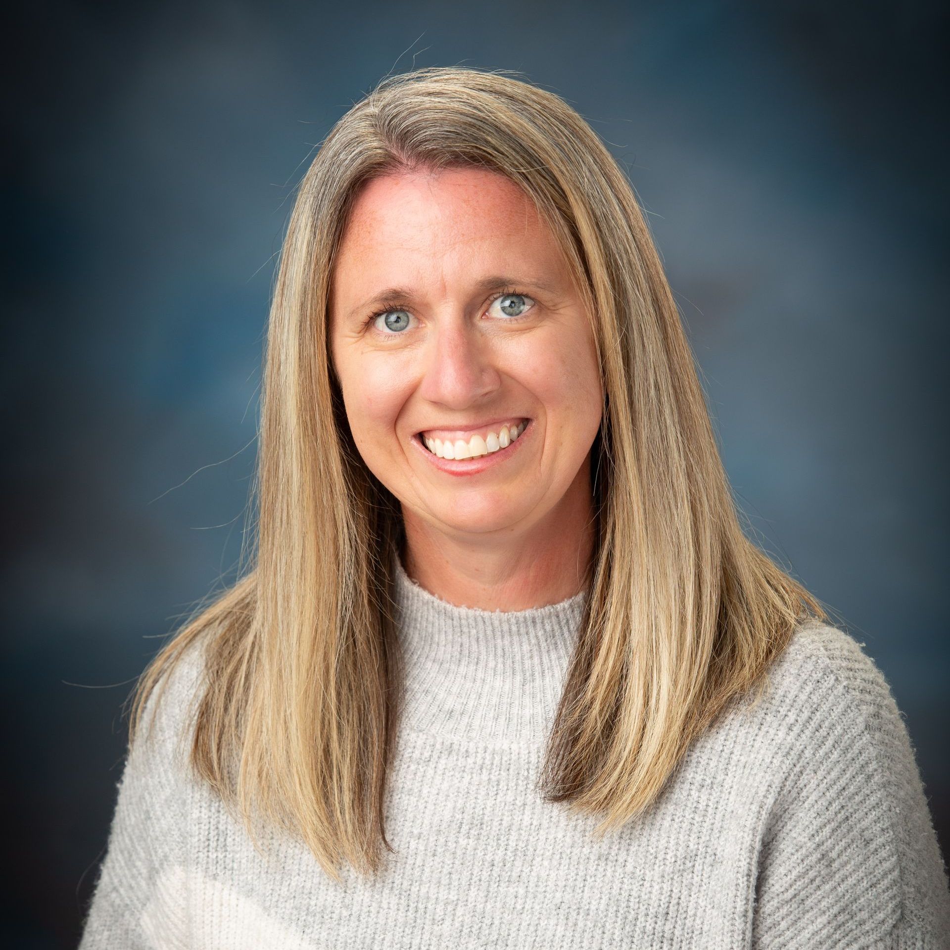 A woman in a grey sweater is smiling for the camera.