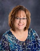 A woman wearing glasses and a blue shirt is smiling for the camera.
