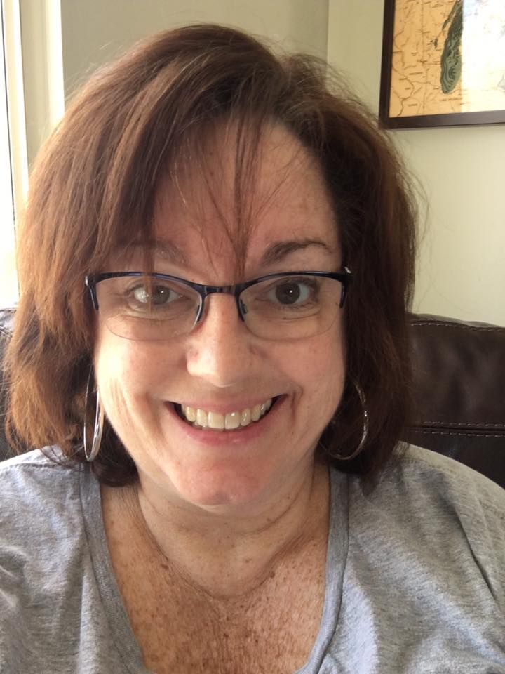 A woman wearing glasses and hoop earrings is smiling for the camera.