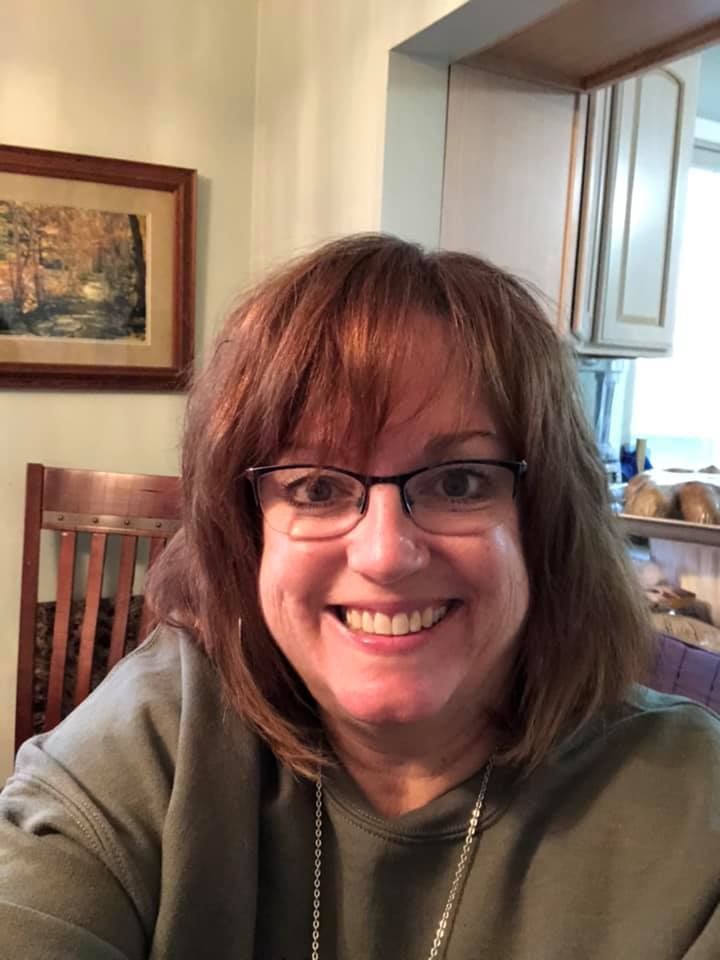 A woman wearing glasses and a necklace is smiling for the camera.