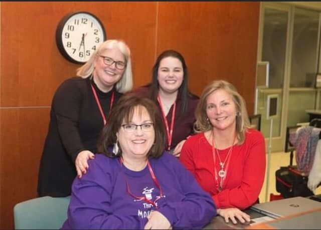 Four women are posing for a picture in front of a clock