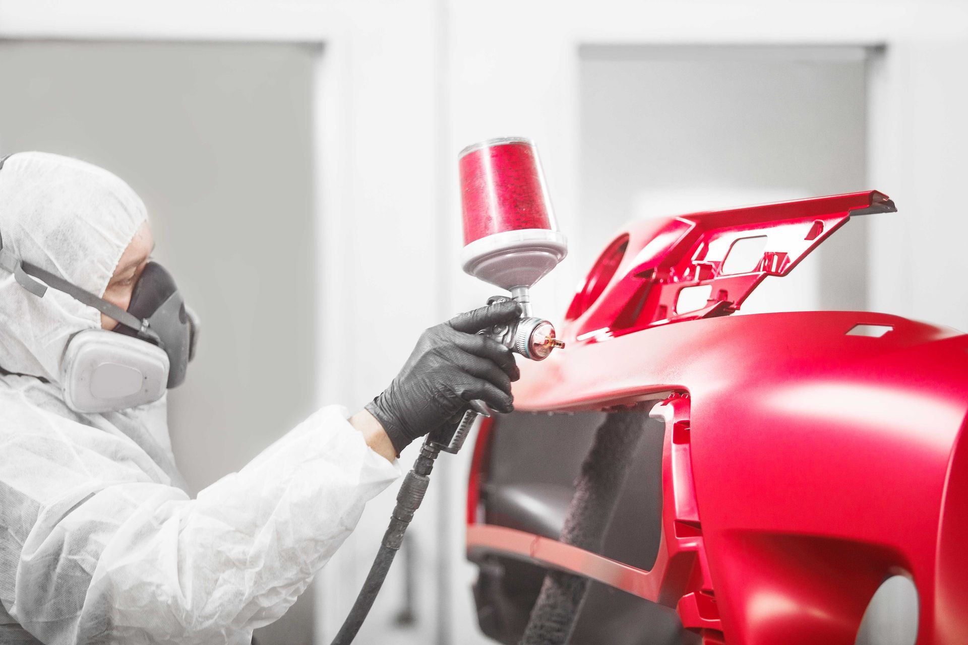 Un uomo con una tuta protettiva sta dipingendo il paraurti rosso di un'auto.
