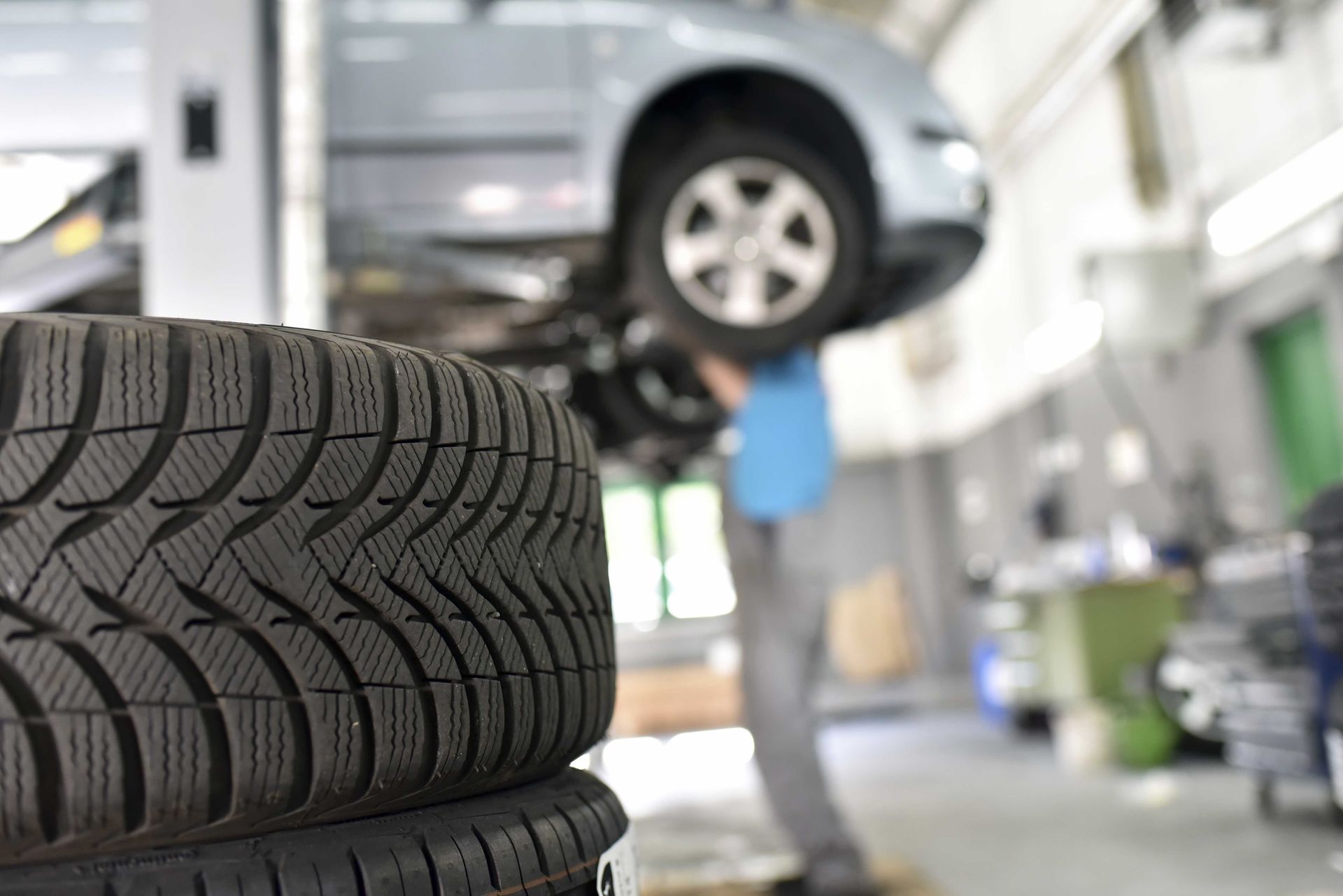 Un primo piano di una pila di pneumatici in un garage con un'auto sullo sfondo.