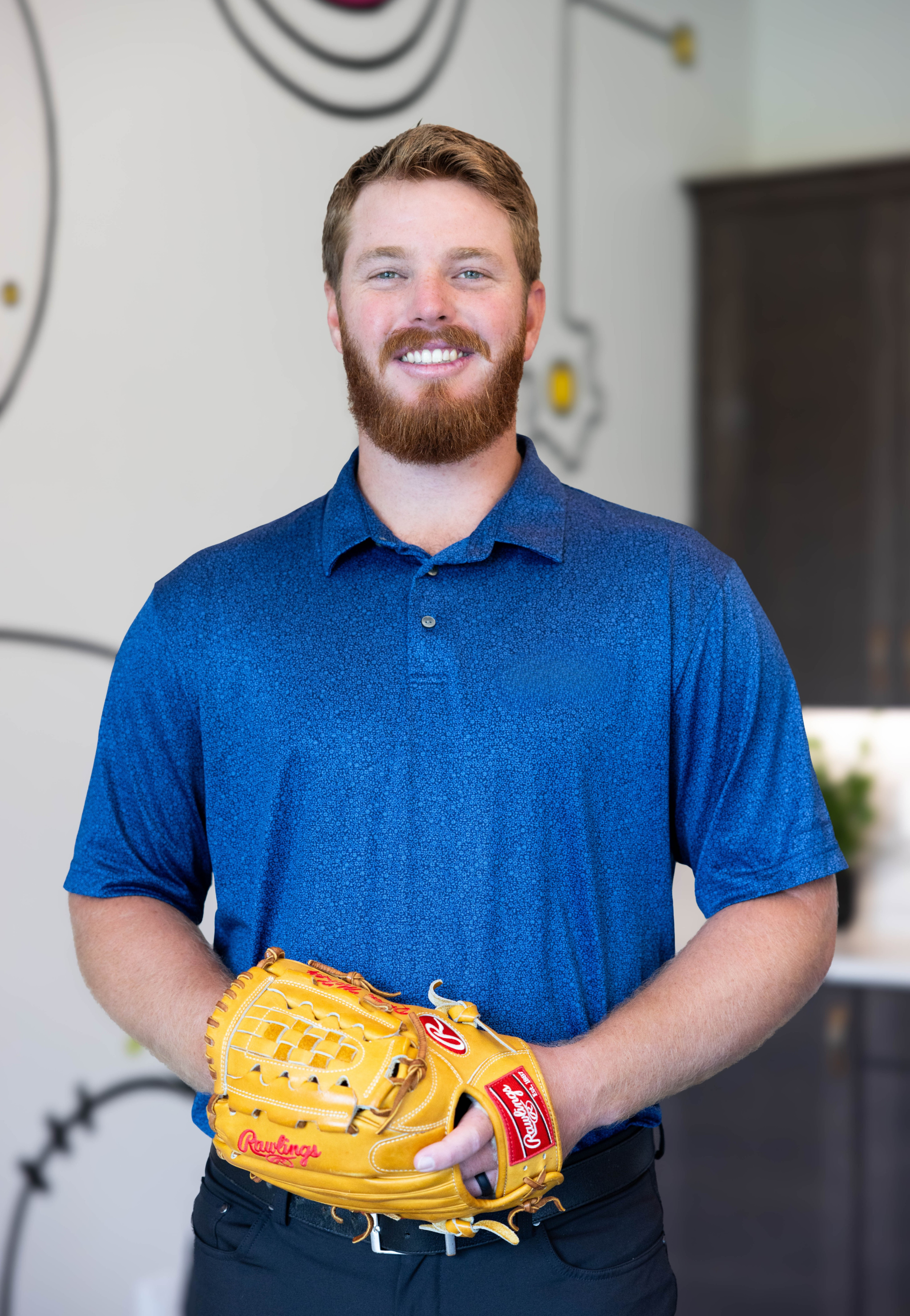 Smiling man in a blue polo holding a yellow baseball glove indoors