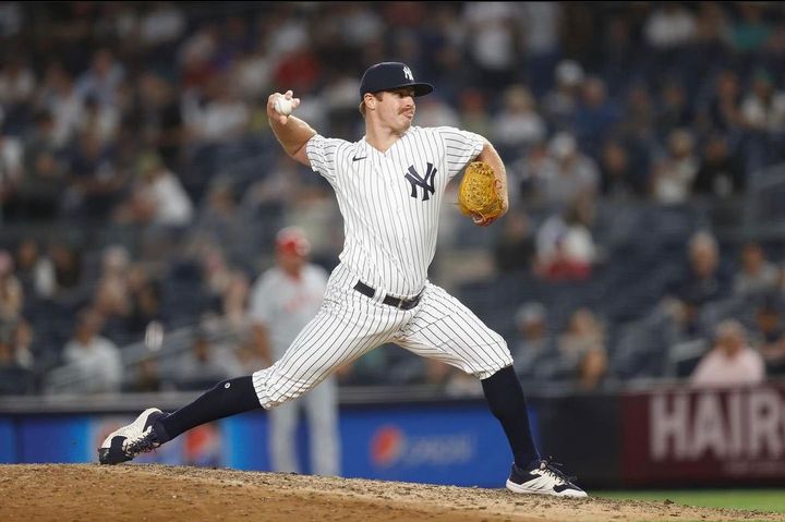 New York Yankees pitcher in pinstripes throwing a pitch on the mound at night