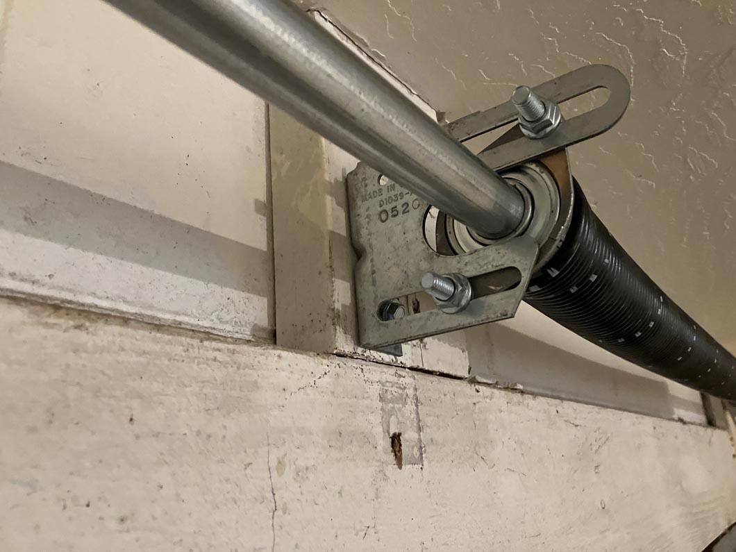 Metal garage door track bracket and spring assembly mounted near the ceiling.