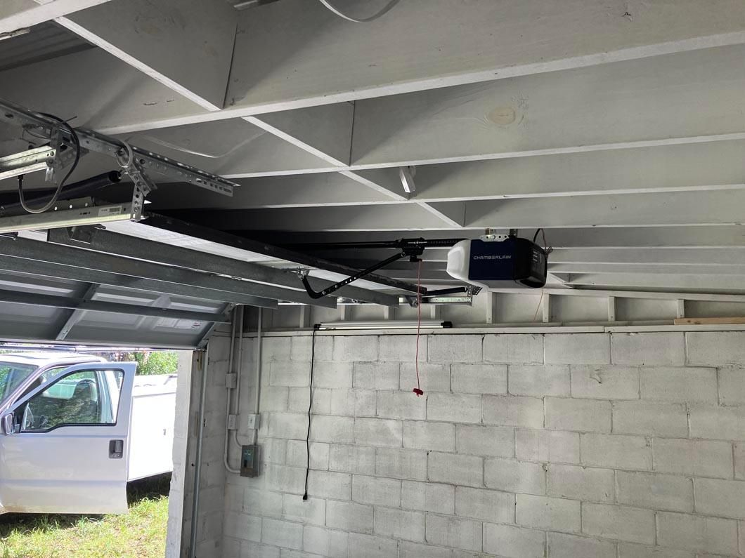 Garage with cinderblock wall, ceiling beams, overhead opener, and a white van parked outside.