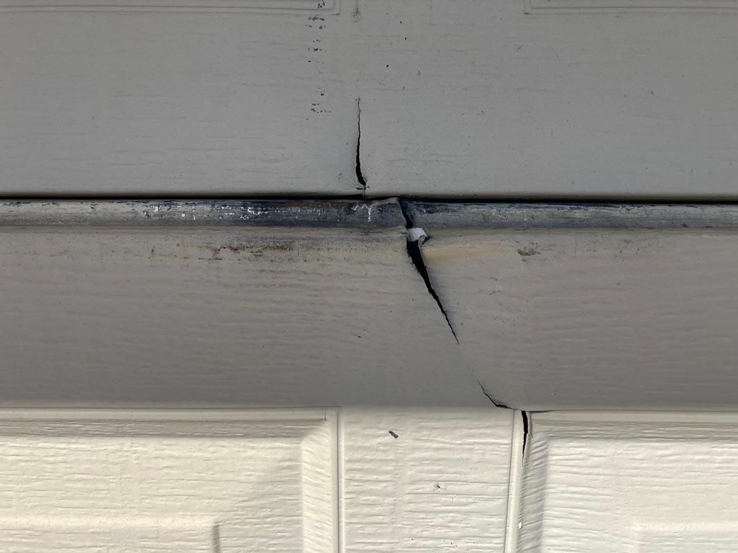 Cracked gray siding above a white wall with a visible gap at the seam