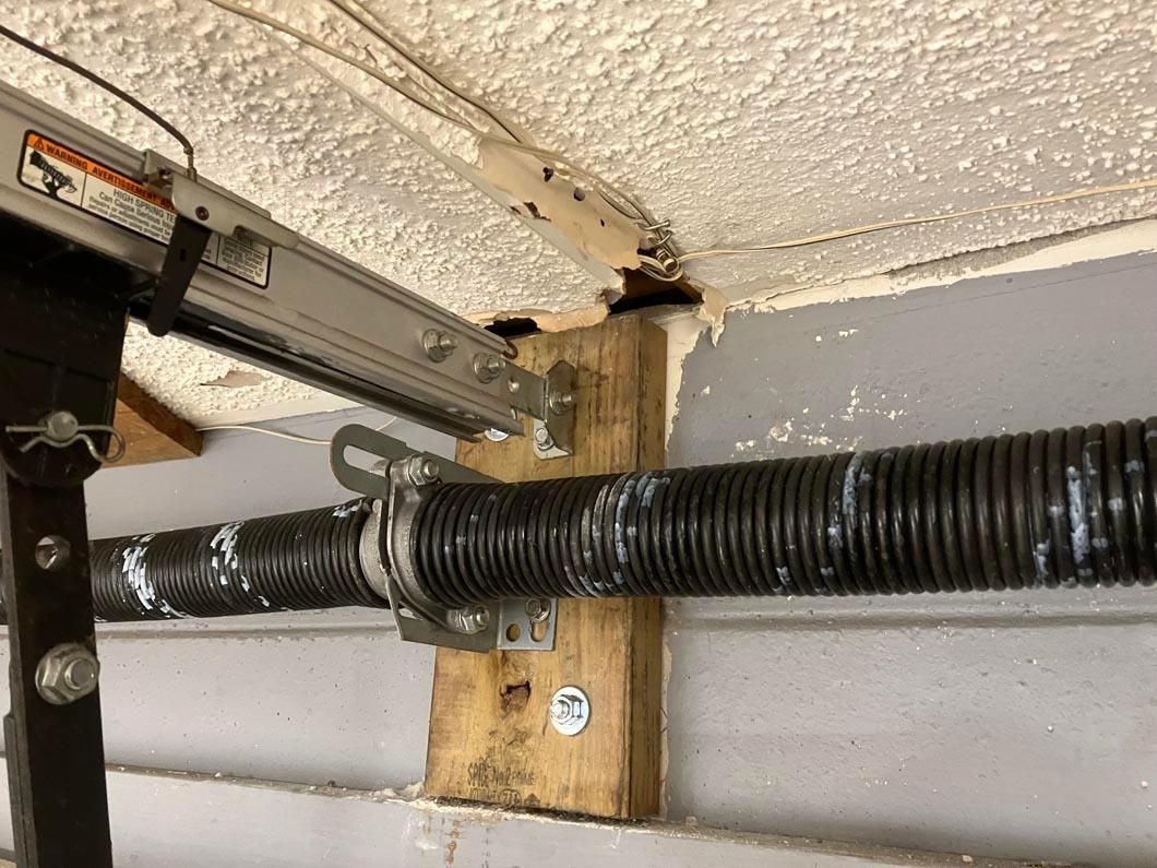 Black corrugated pipe supported by a wooden bracket on a ceiling with rough white insulation.