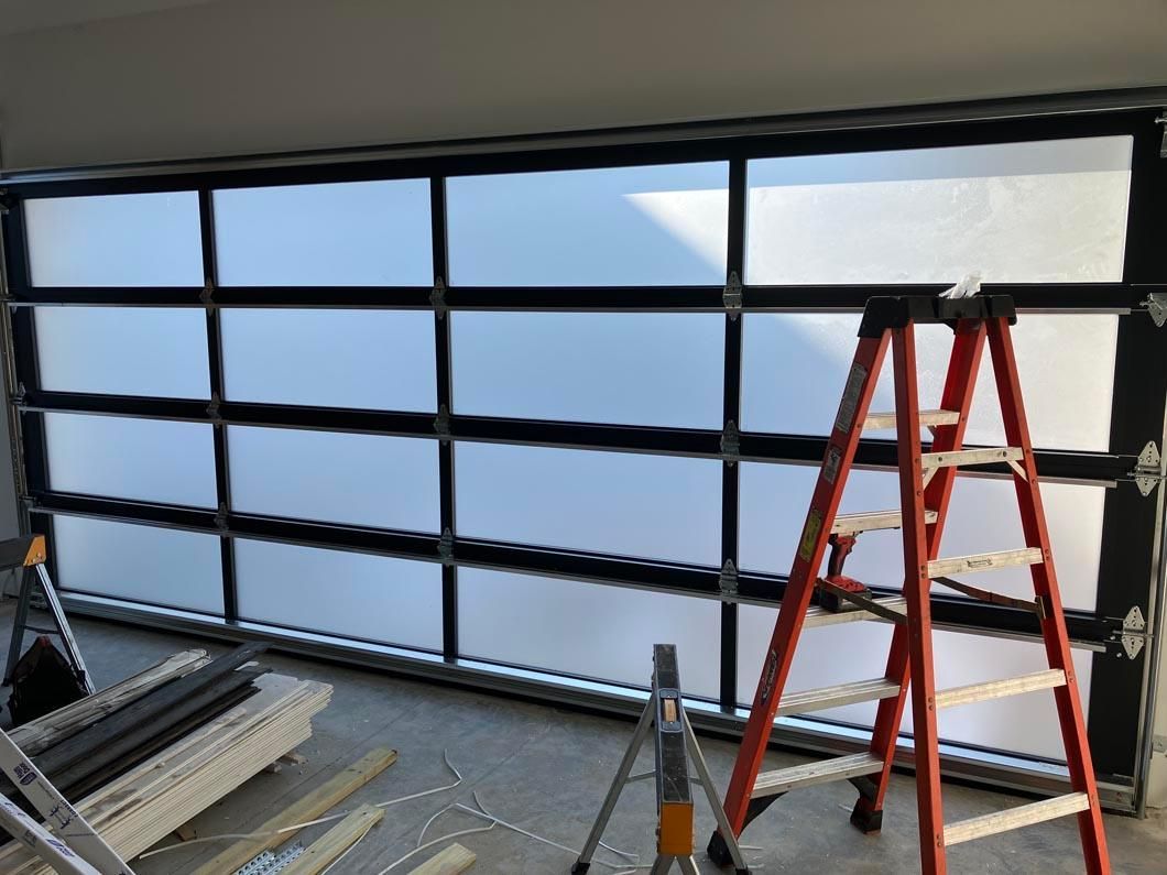 Garage interior with a black framed glass door being installed and a red ladder leaning nearby.