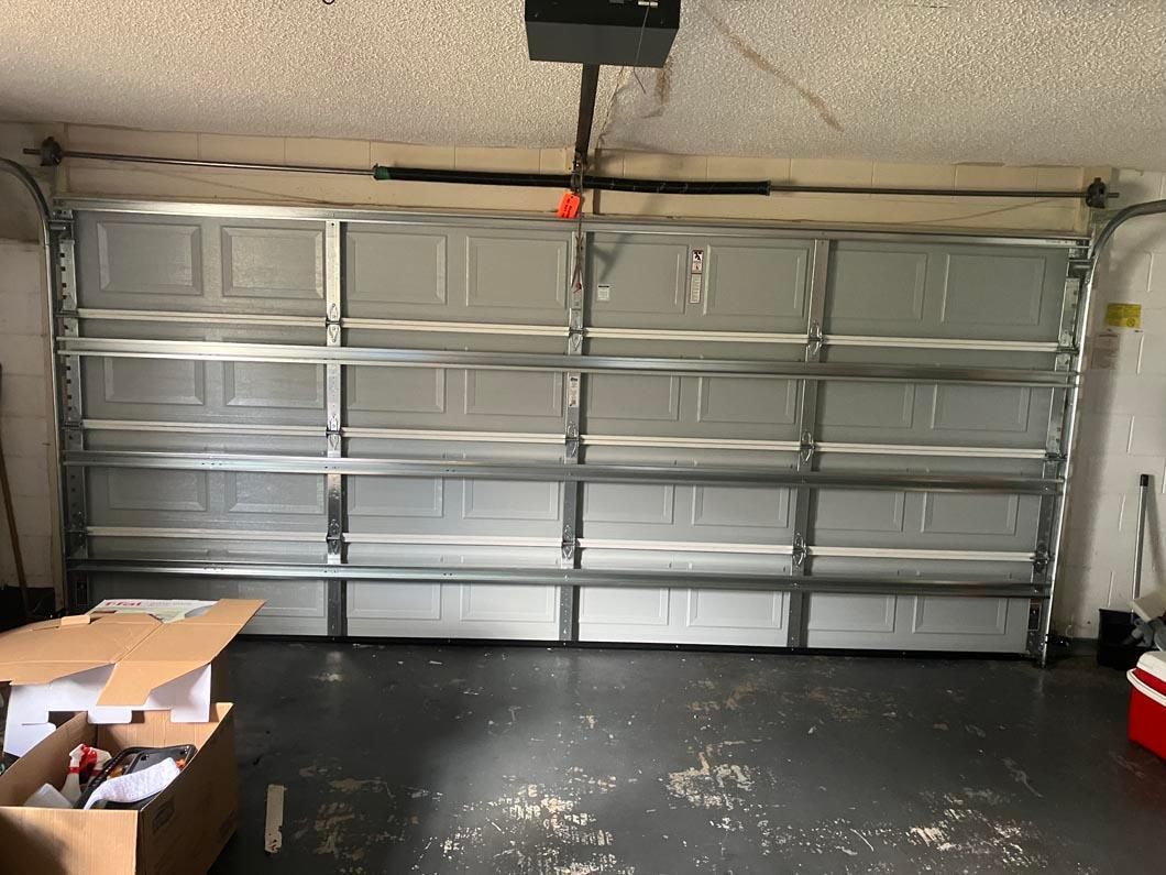 Two-car garage with closed silver sectional door, concrete floor, and boxes in the left foreground