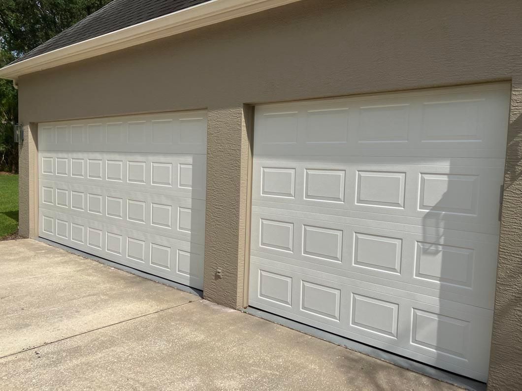 Two white paneled garage doors on a beige house with stone trim and a concrete driveway