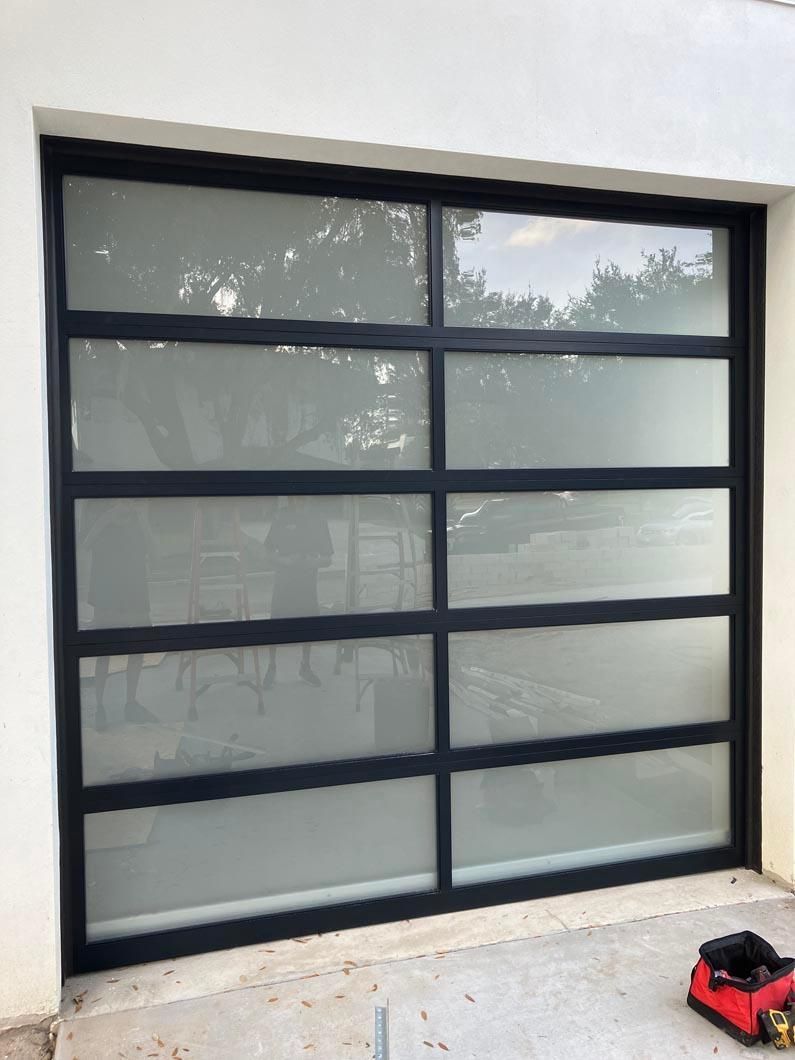 Black-framed glass garage door beside a white wall, with a red and black toy car on the ground