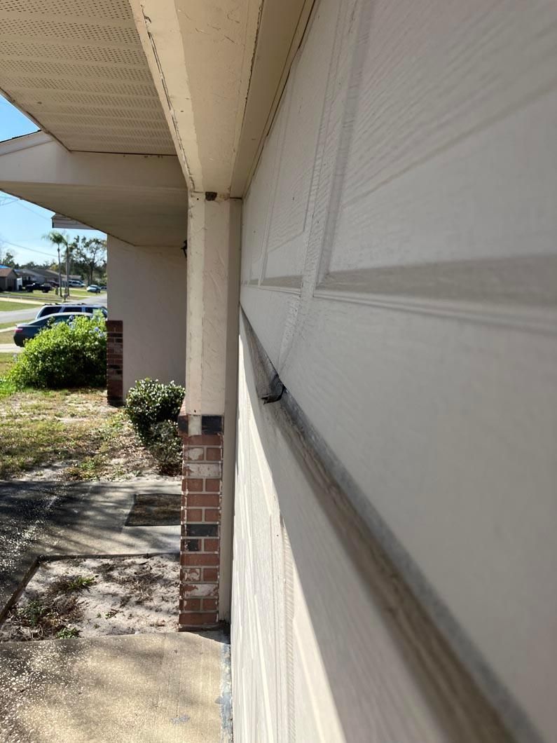 Close-up of a white garage door beside a covered driveway and brick pillar in daylight