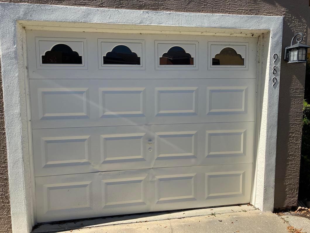 White garage door with four small windows set in a stucco wall, viewed from outside