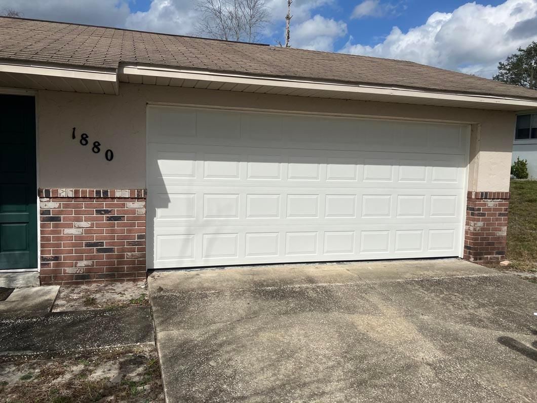 Single-story house exterior with white garage door, tan roof, and brick accents under a blue sky
