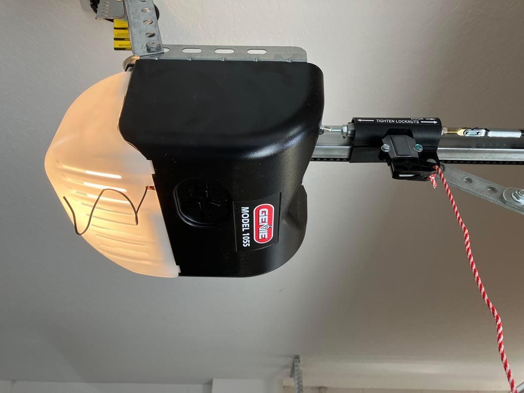 Black garage door opener with attached red cord mounted on ceiling, viewed from below.