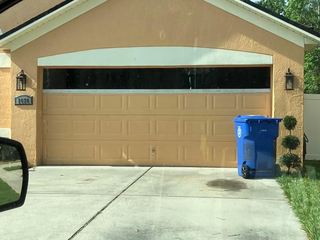 Garage with beige door and blue recycling bin beside a driveway