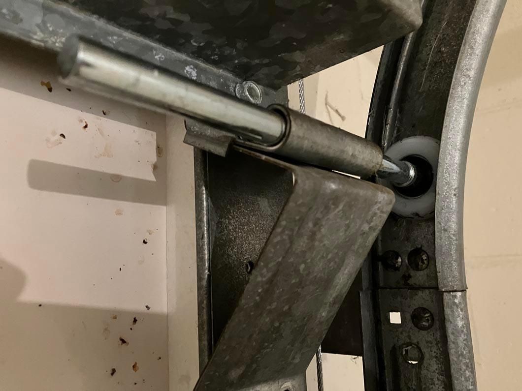 Close-up of a metal pipe and gray bracket attached to a wall, with a black cable running beside it.
