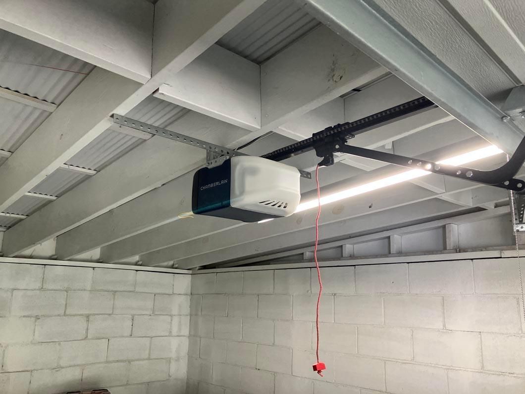 Industrial garage with white cinderblock walls, exposed beams, and a ceiling-mounted garage door opener.