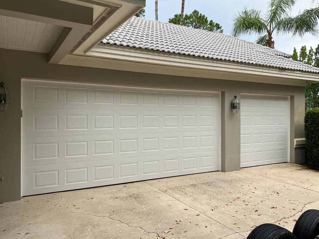 Two white garage doors on a beige house with a tiled roof and concrete driveway
