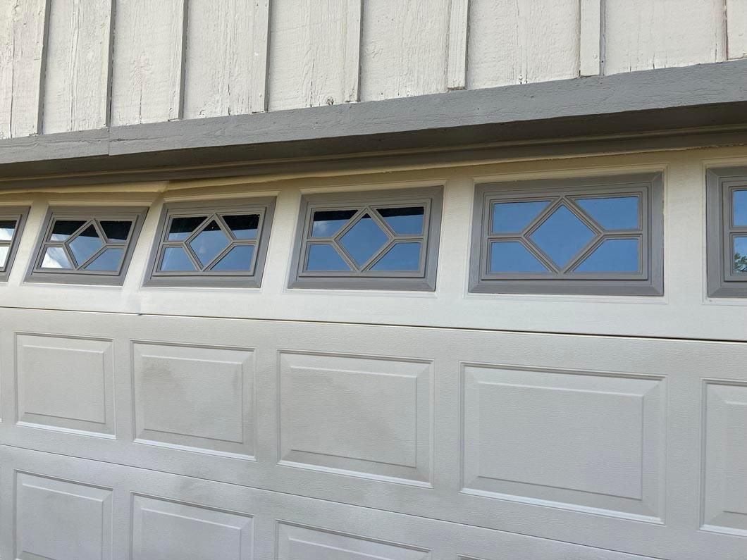 White garage door with decorative window panels on a light gray house exterior
