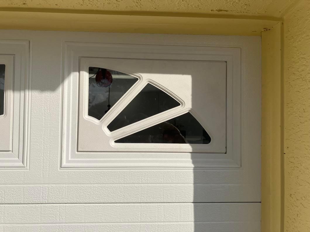White garage door with a broken upper window pane and a yellow exterior wall