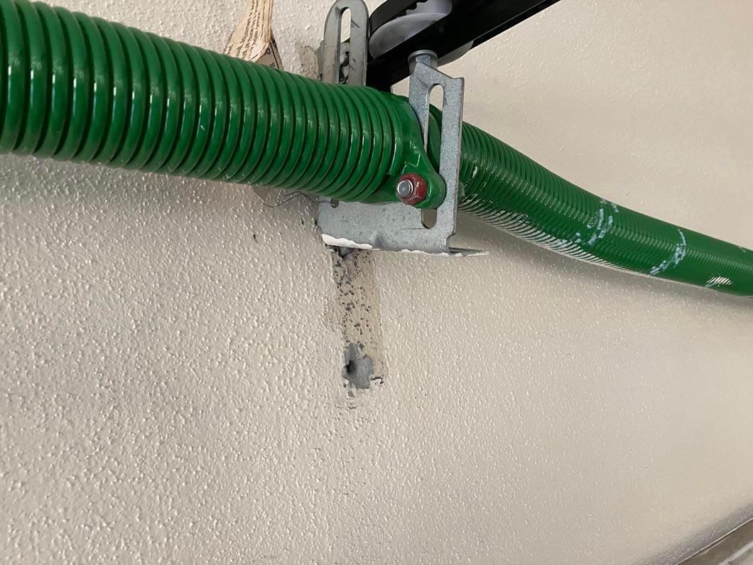 Green corrugated hose secured to a wall with a metal bracket and small red fastener.