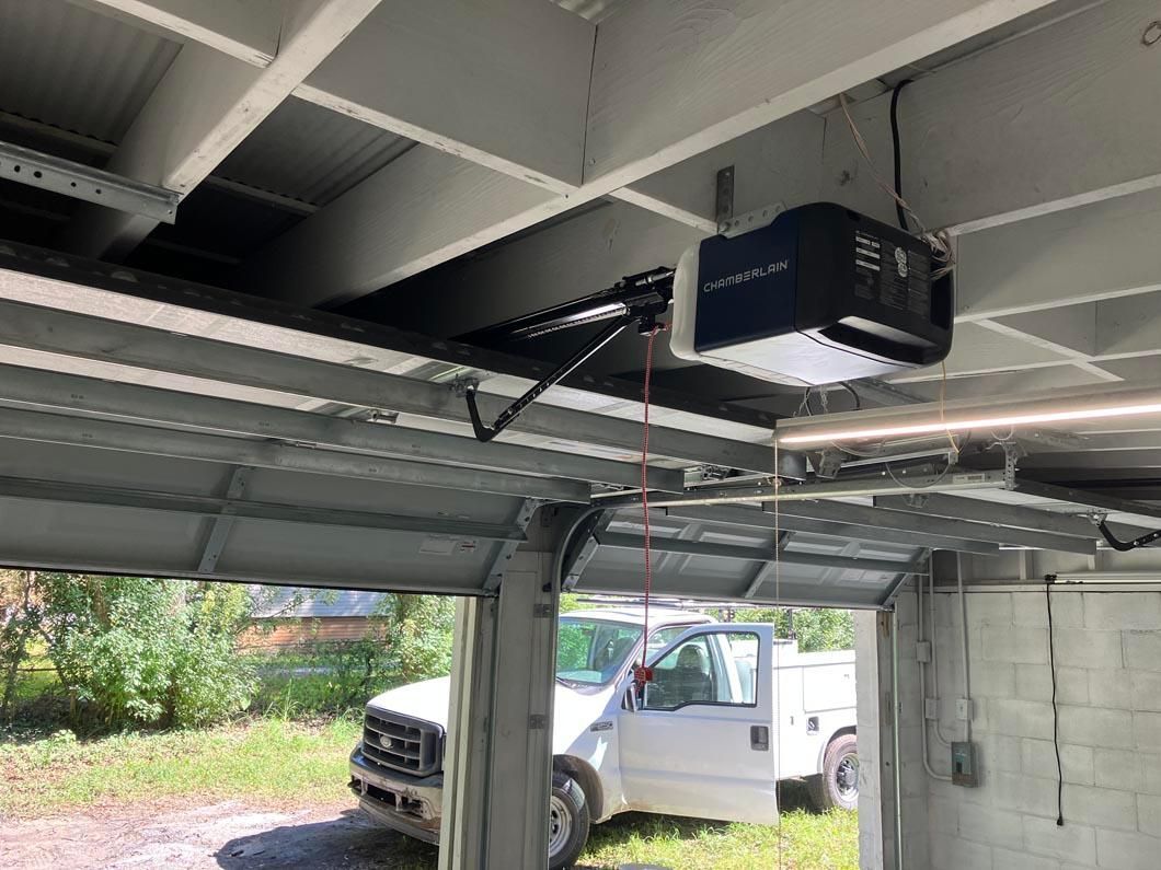 Garage door opener mounted on a ceiling beam, with a white truck parked below.