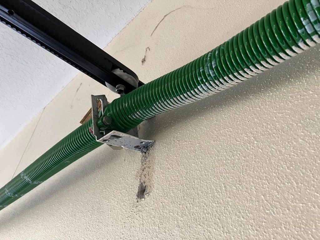Green coiled hose mounted to a ceiling bracket with a small hanging tool or nozzle below
