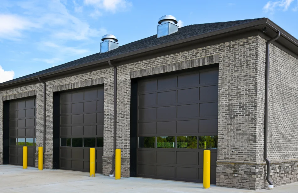 Brick industrial building with three dark garage doors and yellow bollards at the front