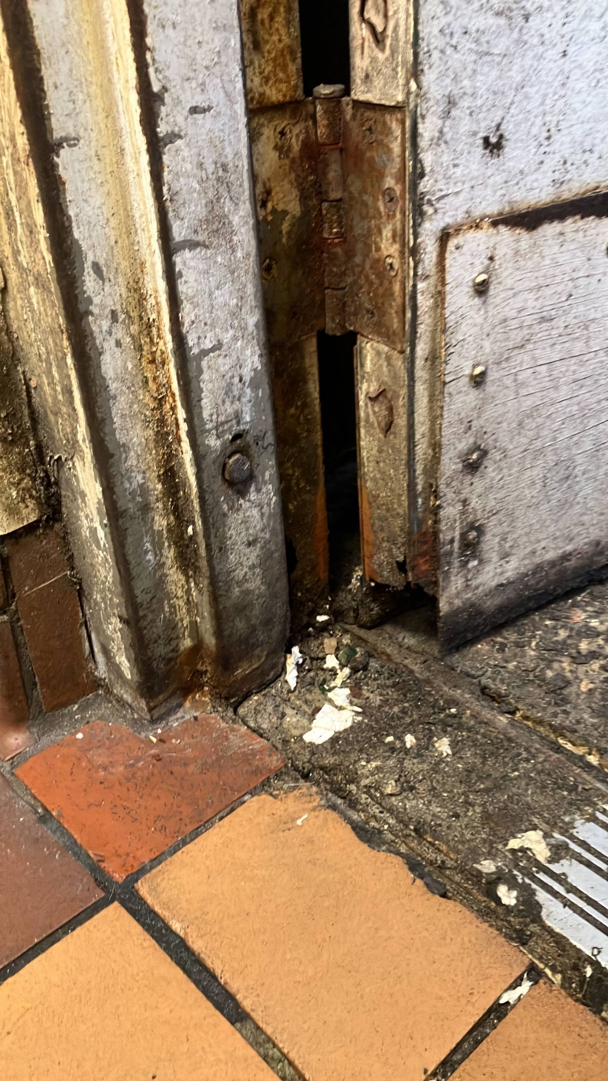 Rusty damaged door bottom with a gap and worn floor tiles beside it