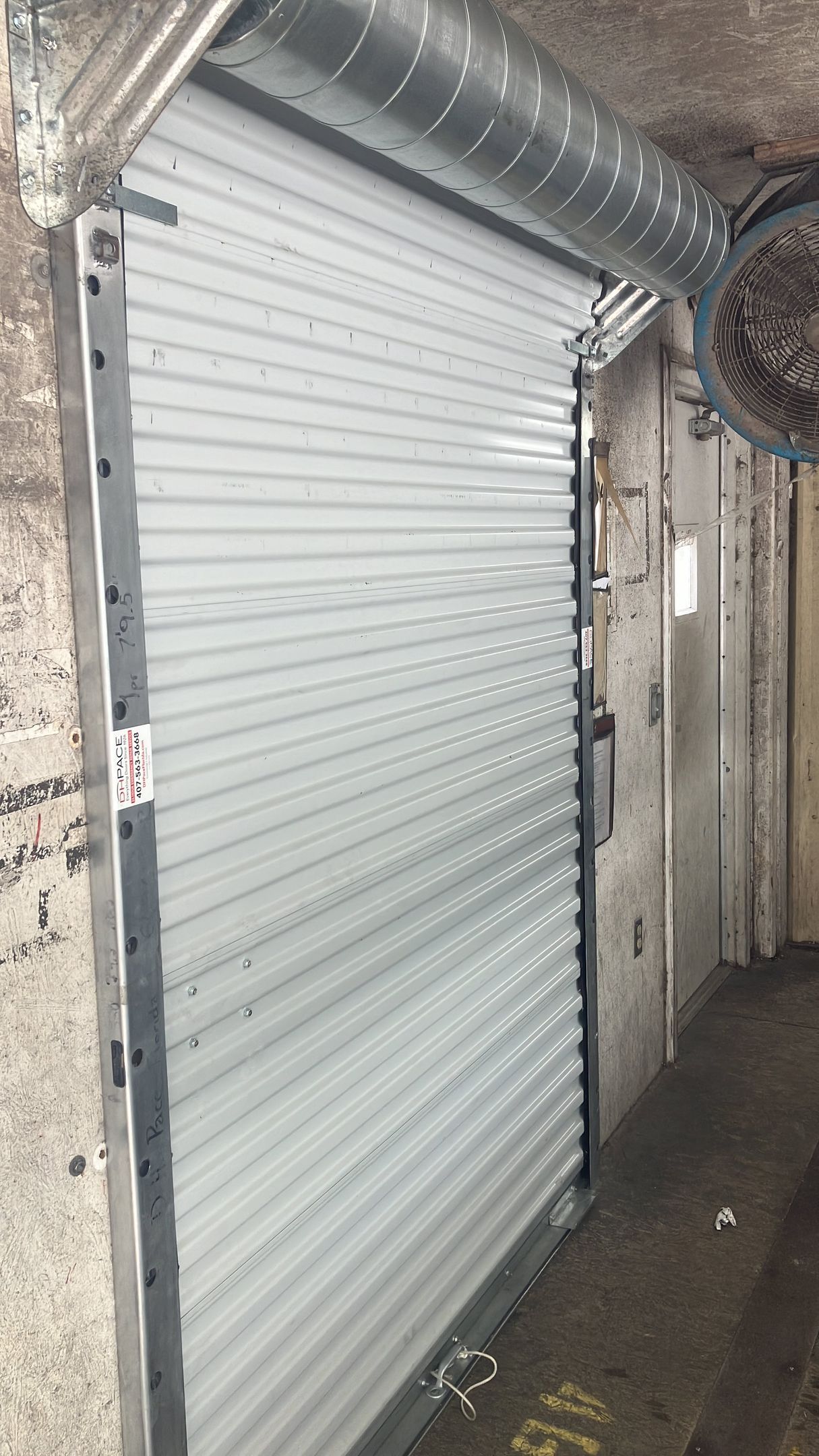 Closed white roll-up metal door in a narrow concrete corridor￼