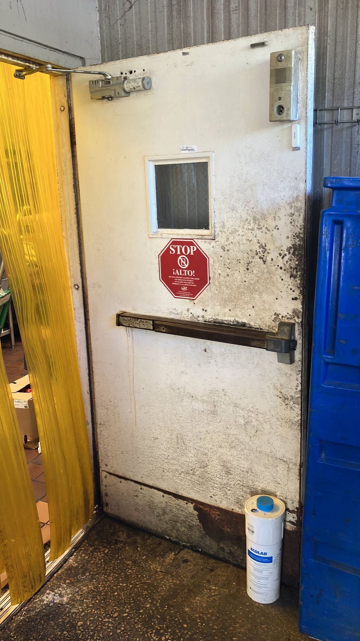 White industrial door with a small window, red stop sign, and side latch in a warehouse corridor