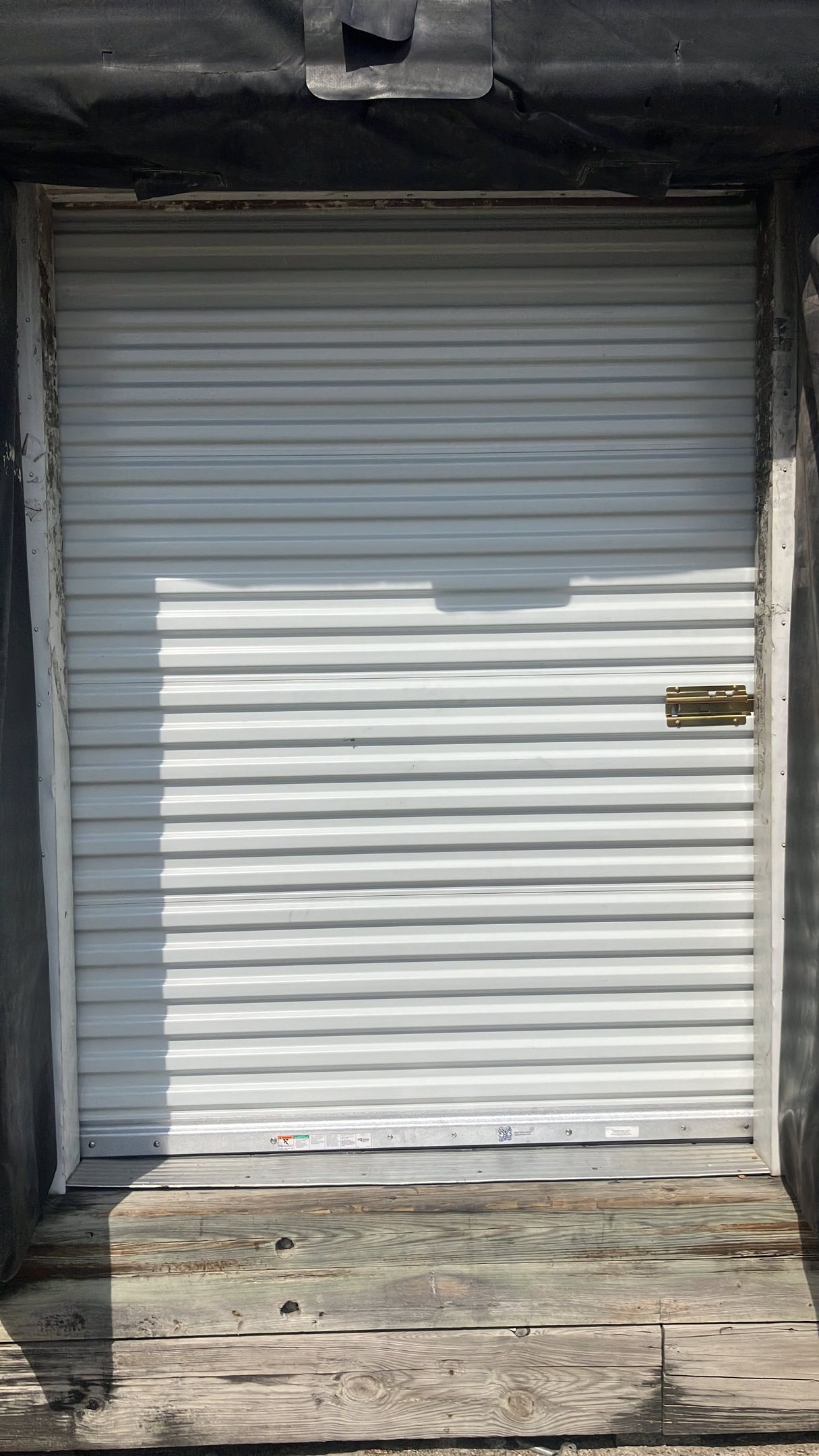 Closed white metal roll-up door with a small handle on the right, framed by a dark doorway.