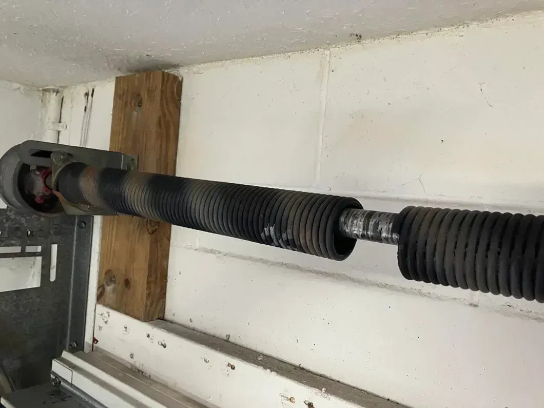 Black corrugated pipe with metal couplings running through a white wall near a wooden support beam