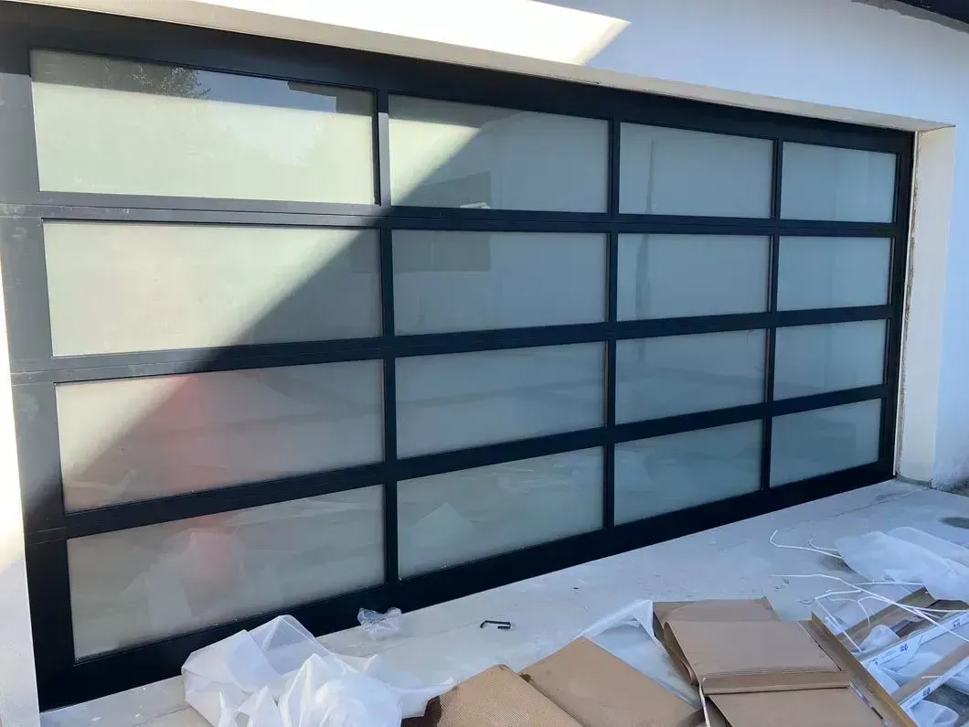 Black-framed frosted glass garage door installed in a bright room, with construction materials on the floor