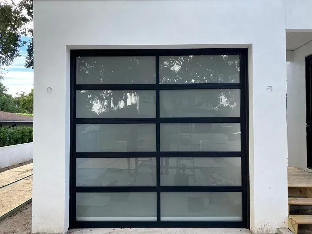 Modern black-framed glass garage door set in a white exterior wall