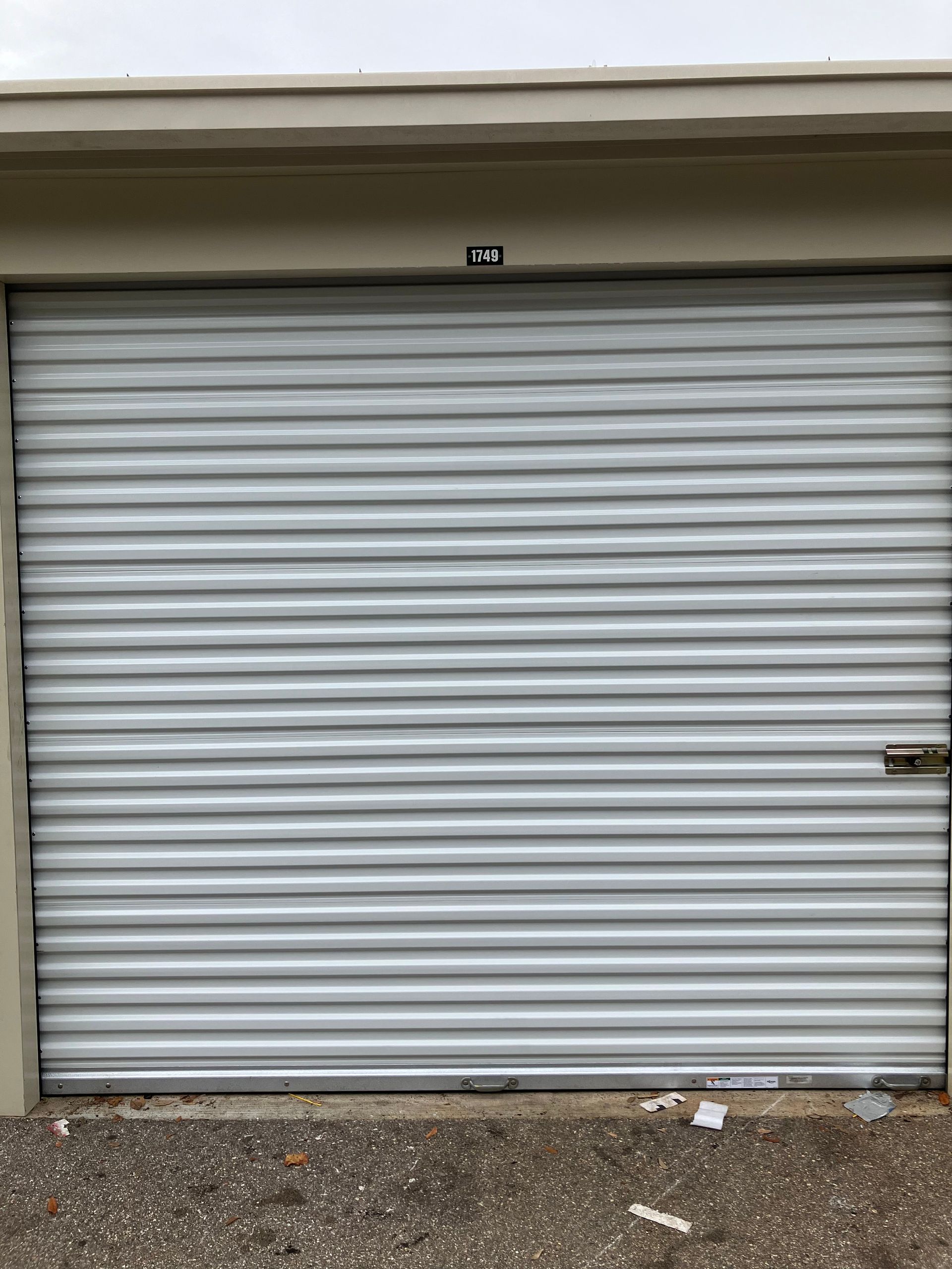 Closed silver metal roll-up garage door with a small keypad above it and gravel below