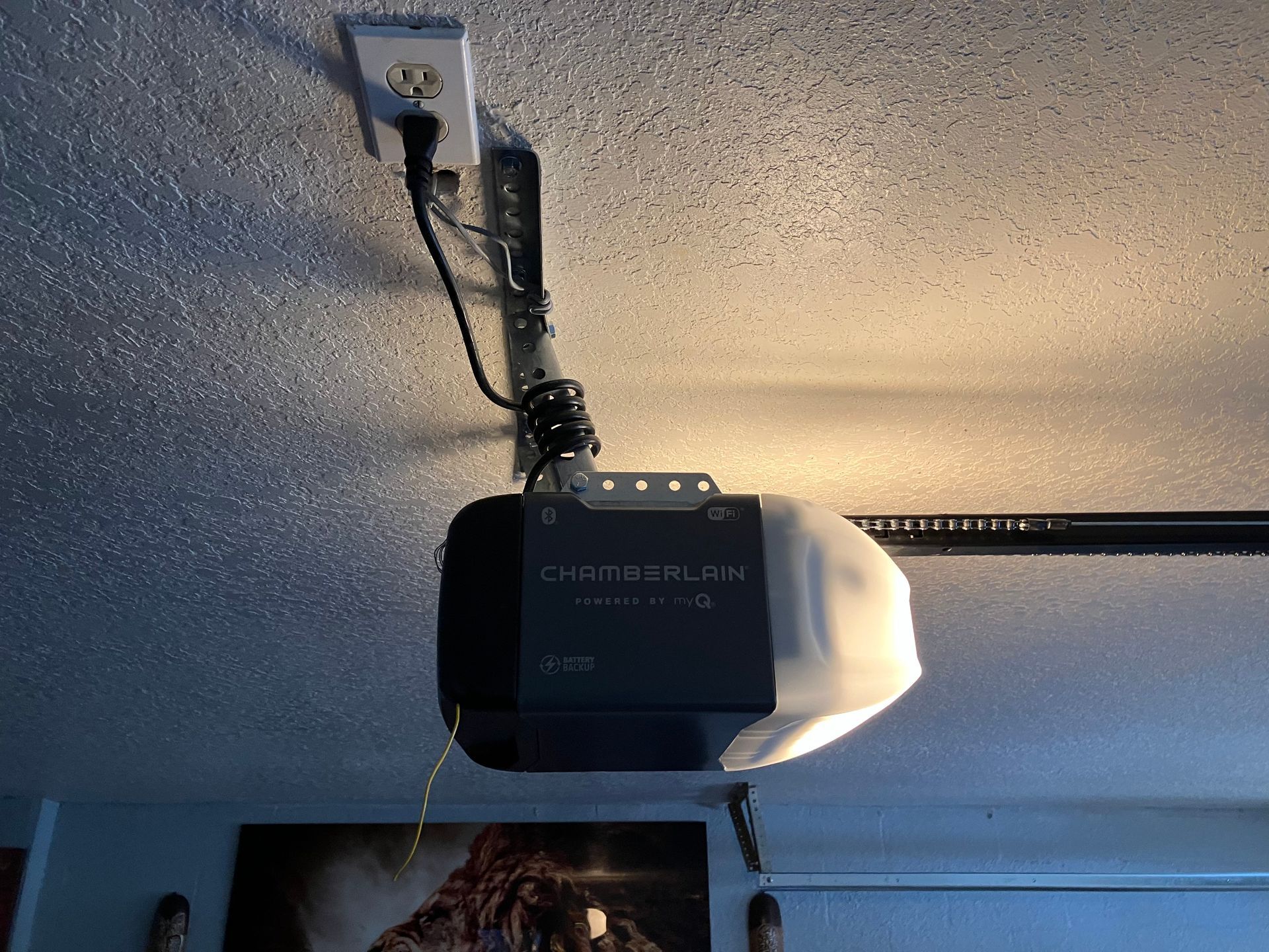 Garage door opener mounted on a ceiling, with cords and a ceiling outlet visible.