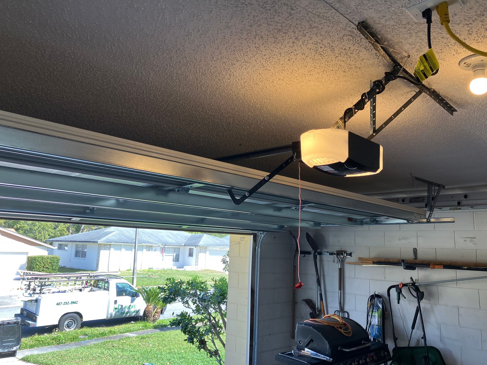 Open garage door showing a white truck outside, with garage ceiling lights and storage equipment inside