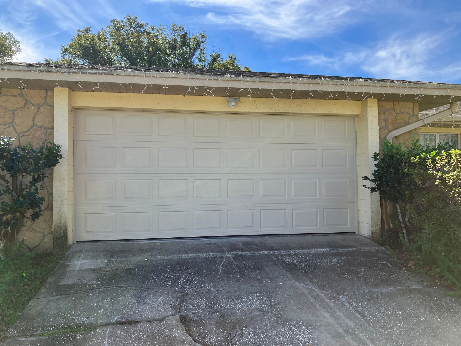 White garage door at the end of a concrete driveway beside a beige house, under a blue sky.