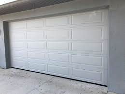 White garage door on a gray exterior wall and concrete driveway