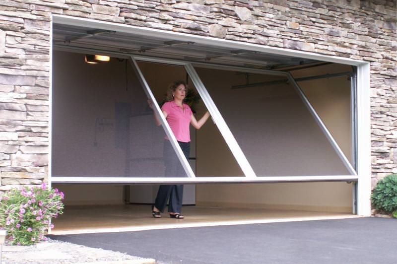 Woman standing in a partially opened garage door with slanted glass panels in a stone house facade