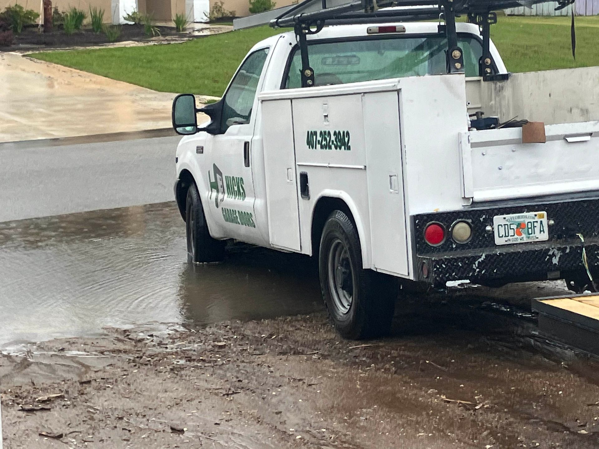 White utility truck parked on a wet residential street after rain, viewed from the rear side.